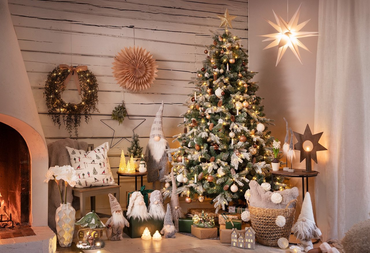 Jouluaiheinen olohuone, jossa kuusi, tonttuja ja takkatuli tunnelmallisessa ympäristössä.