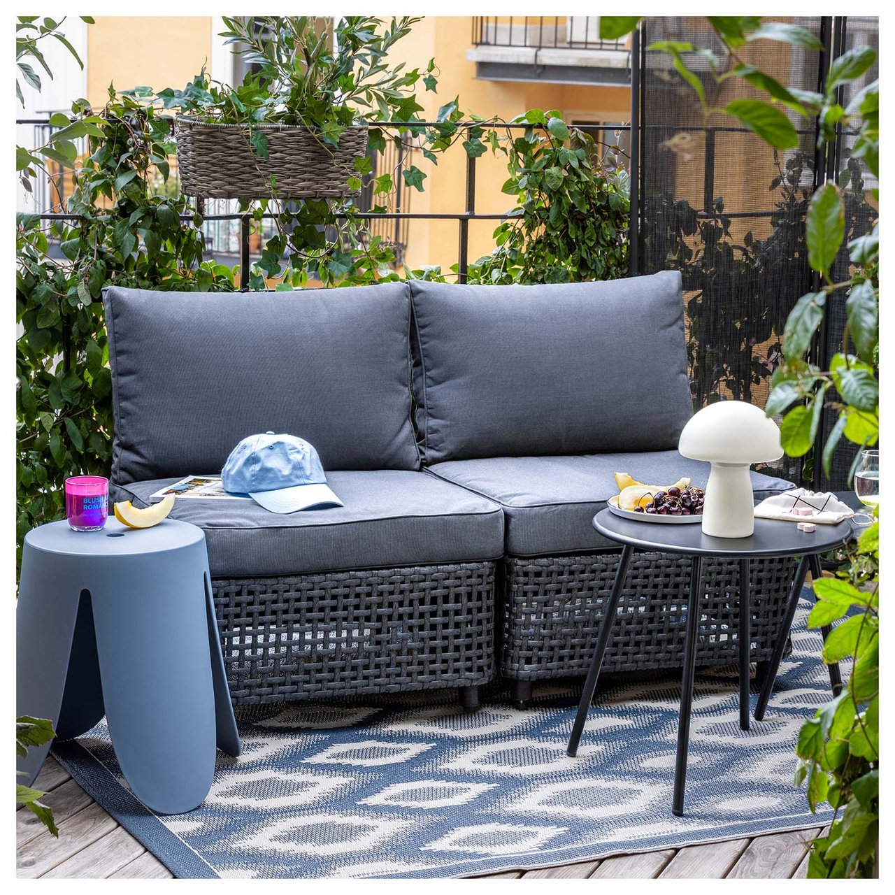 En grå toseters sofa i rotting på en balkong. Ved siden av og foran sofaen står det små bord.