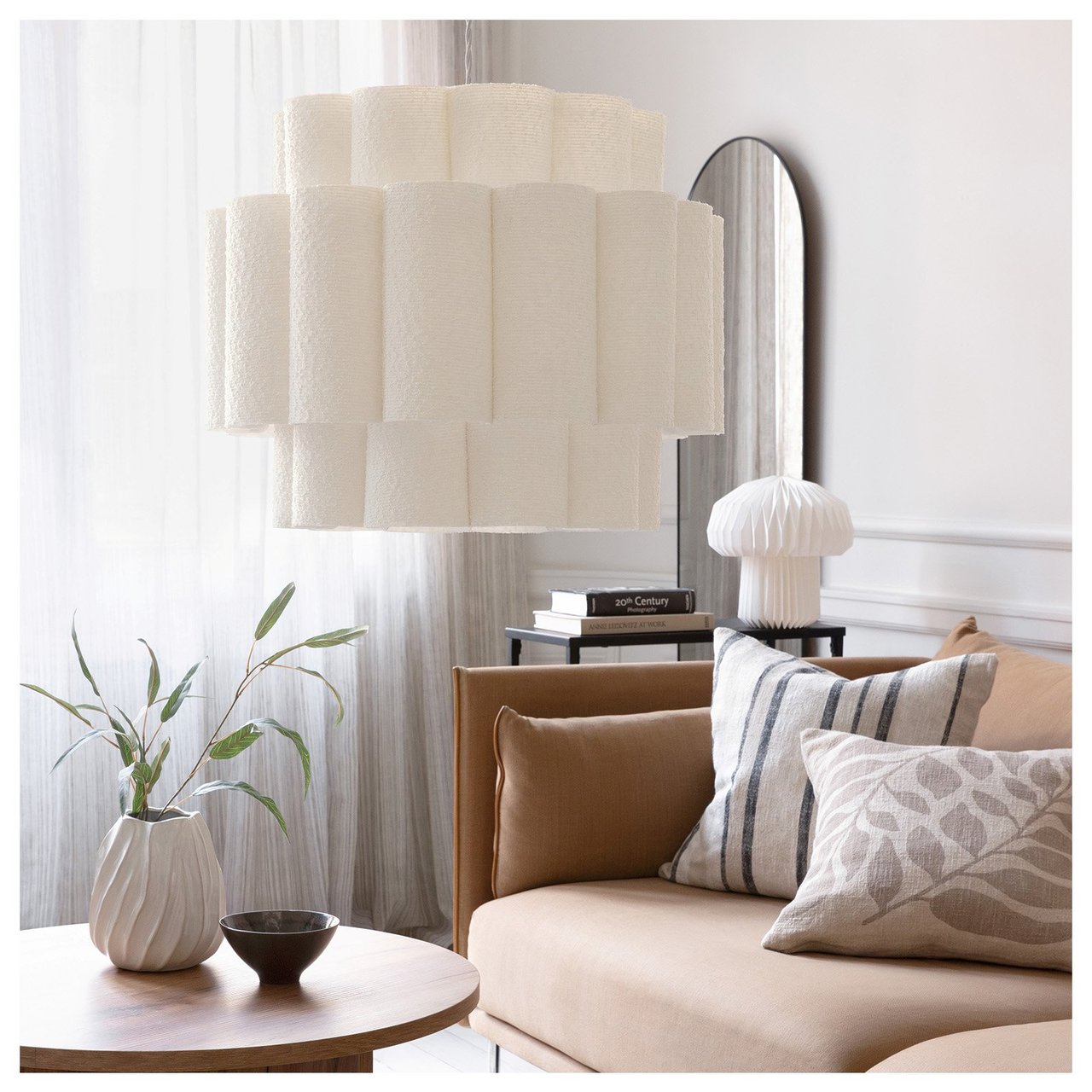 En hvit, bølgeformet taklampe med tekstilskjerm henger i en stilren stue.