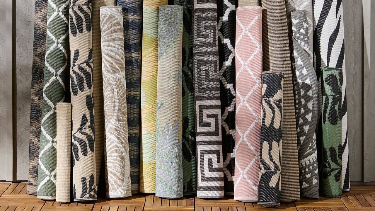 Ett stort antal mönstrade och ihoprullade utomhusmattor lutar mot en husfasad.