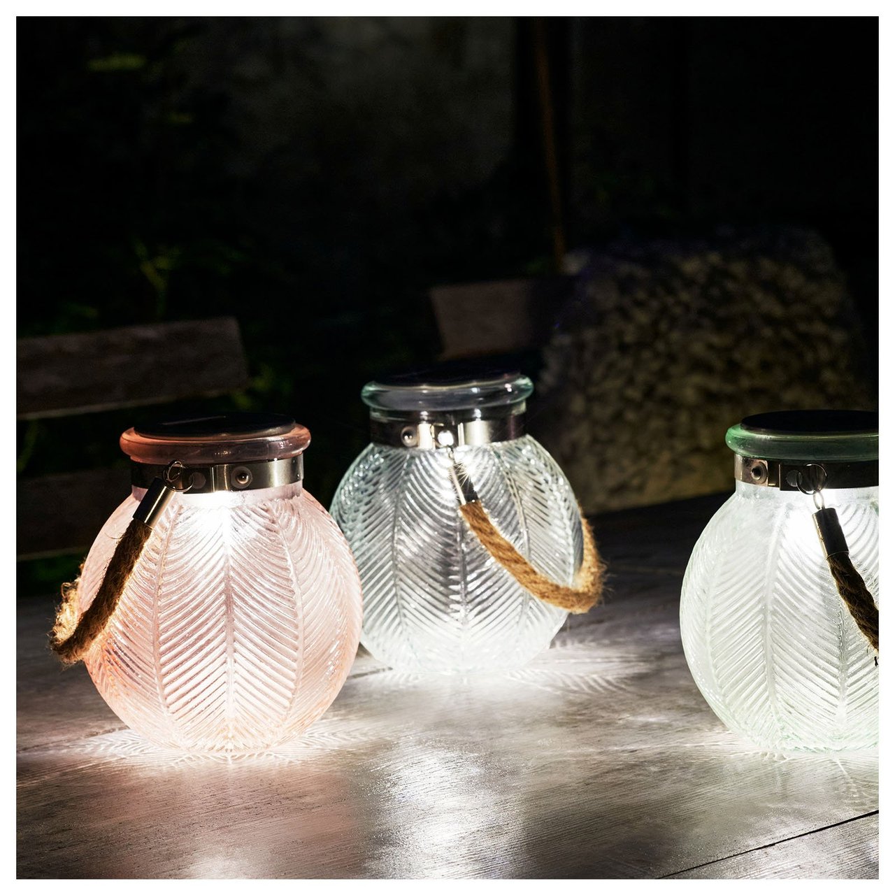 Drei pastellfarbene Solarlampen leuchten auf einem Tisch im Dunkeln.