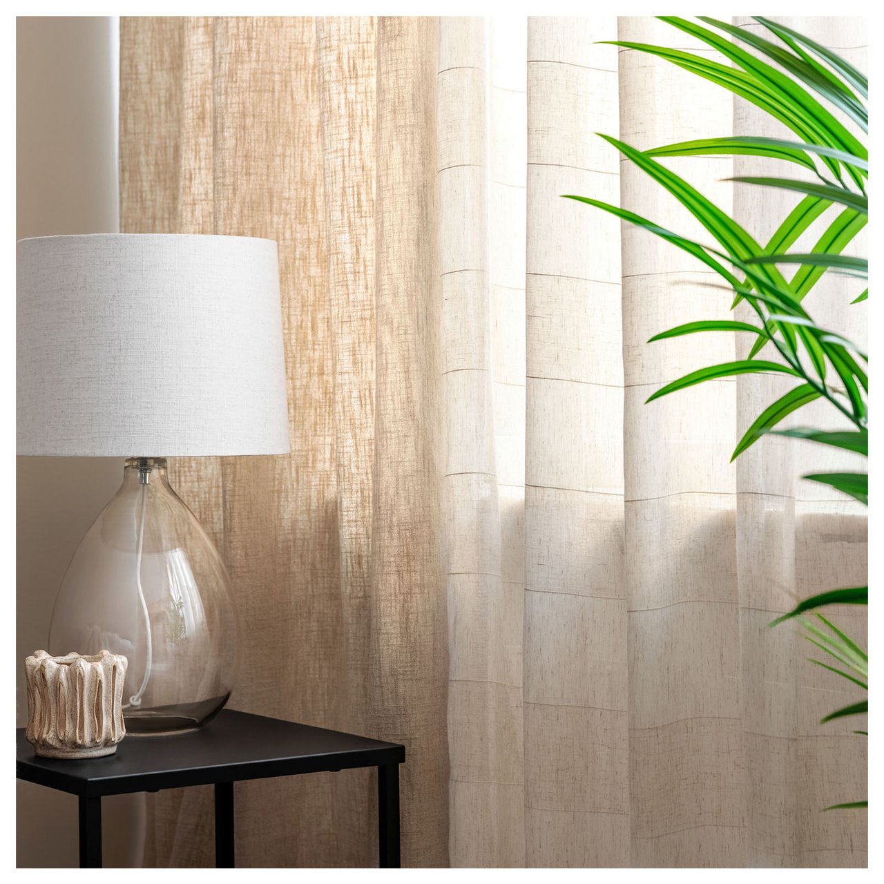 Beistelltisch mit Tischlampe am Fenster mit hellen Vorhängen und grüner Pflanze.