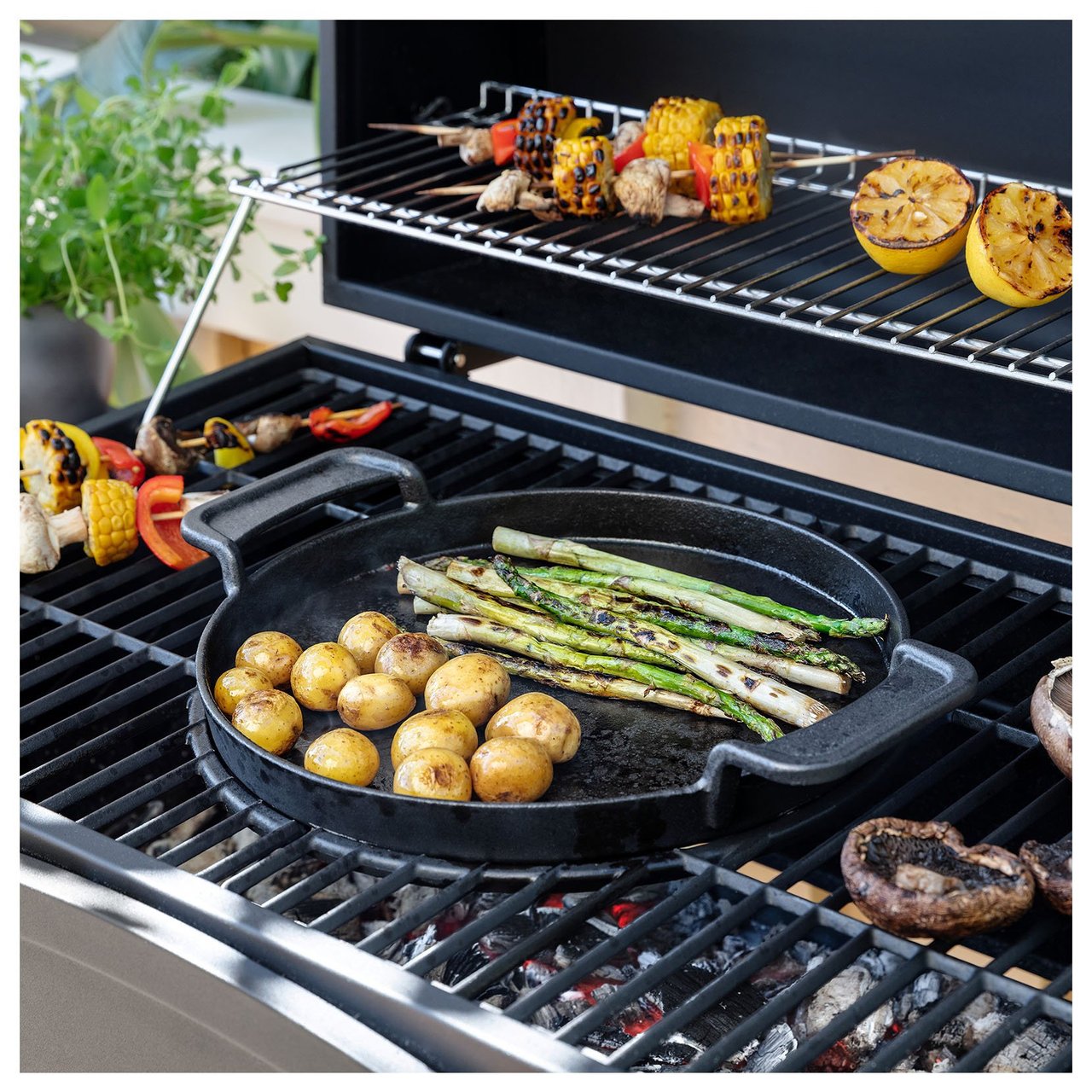 Nahaufnahme von Kartoffeln und Spargel in einer Gusseisenpfanne auf einem Grill.