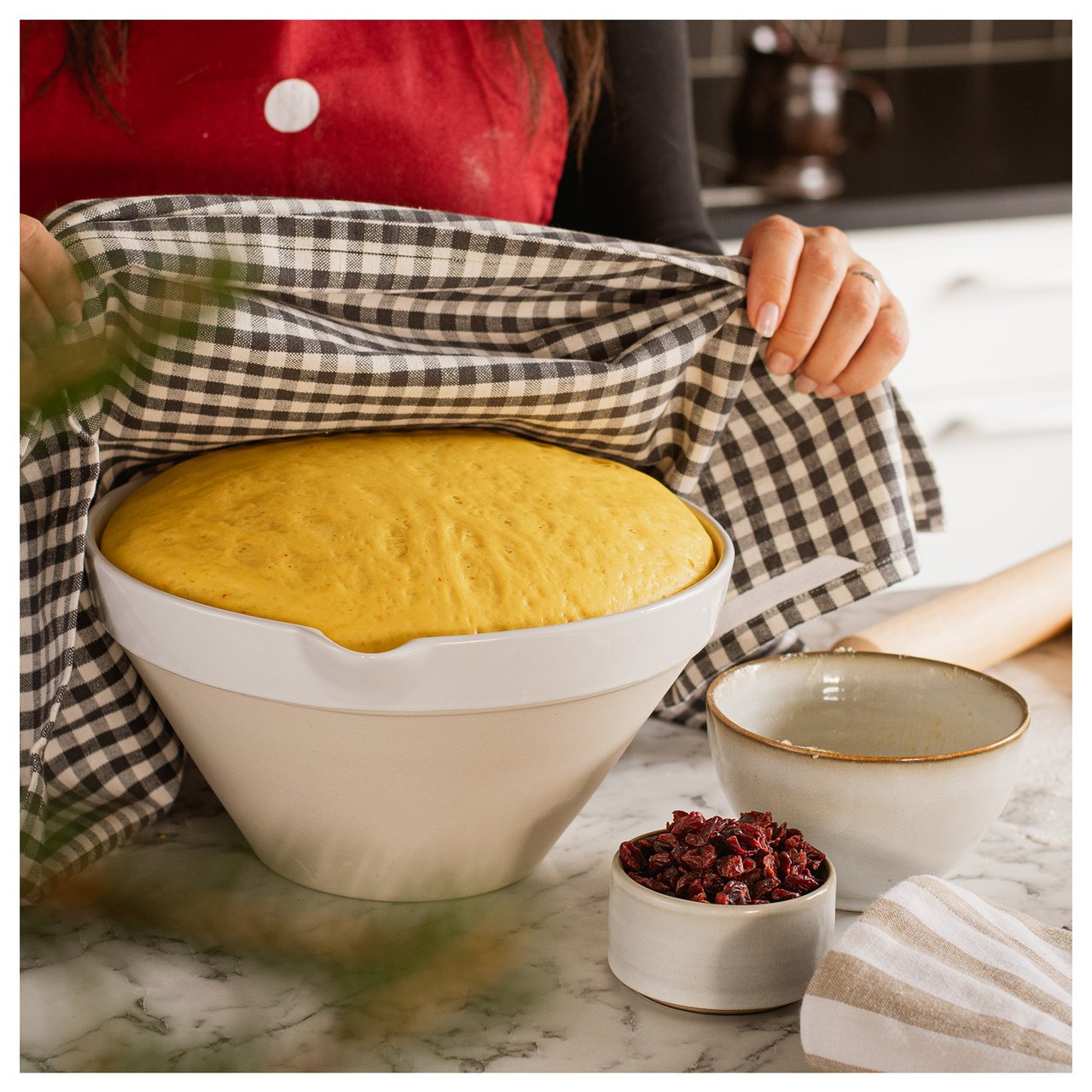 Safranteig, der in einer Schüssel geht. Eine Person bedeckt ihn mit einem karierten Geschirrtuch.