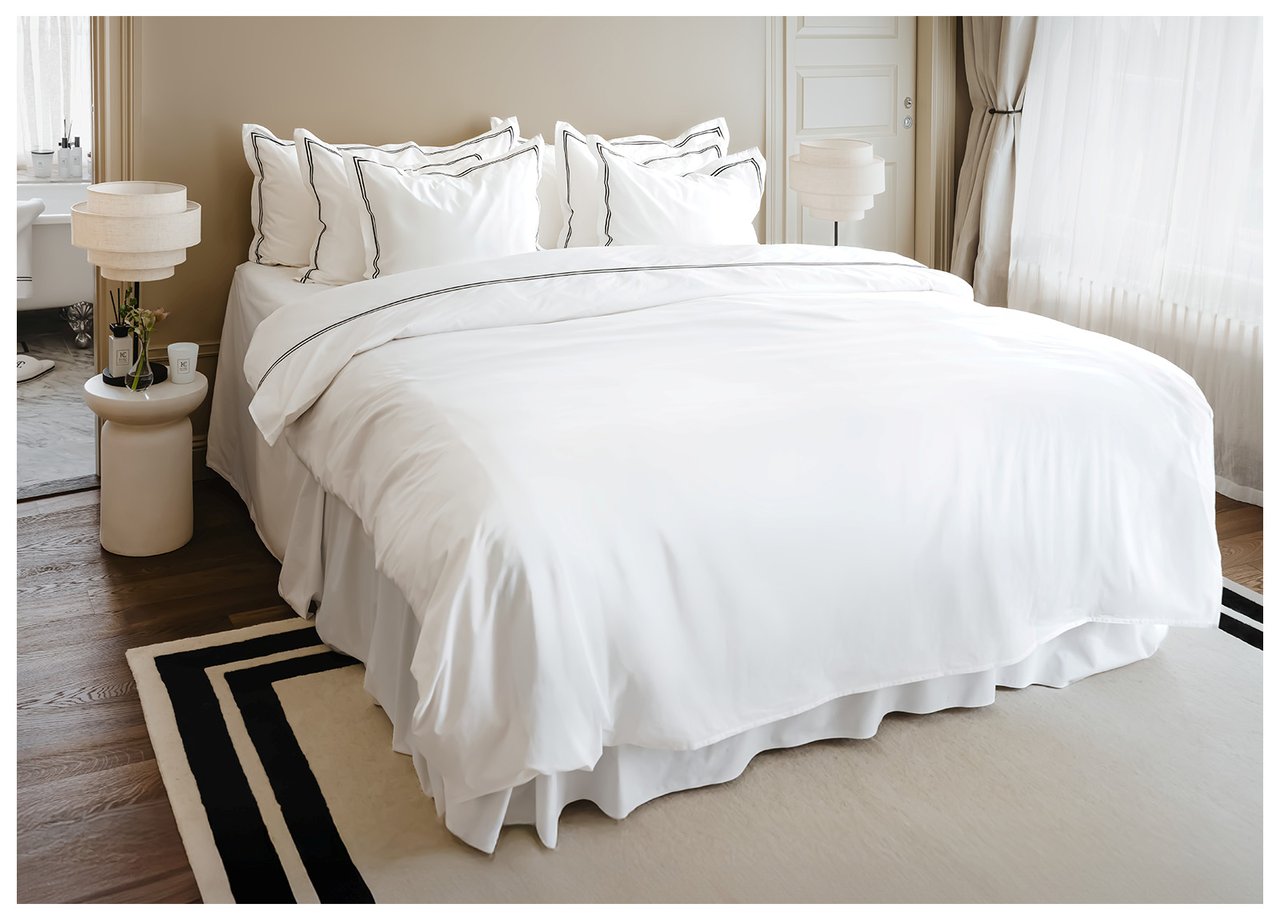 Doppelbett mit weißer Bettwäsche und vielen Kissen. Großer Teppich unter dem Bett. Nachttische mit weißen Lampen.