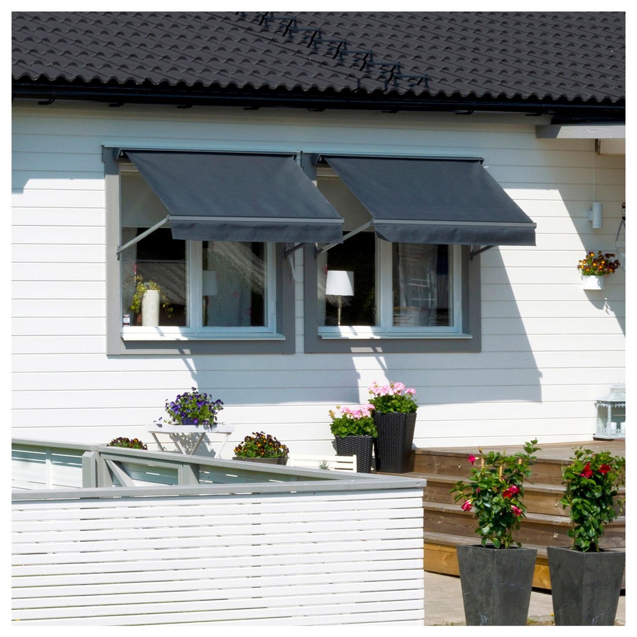 Närbild på två fönster med gråmålade karmar mot vit fasad. Fönstren har utfällda mörkgrå markiser.