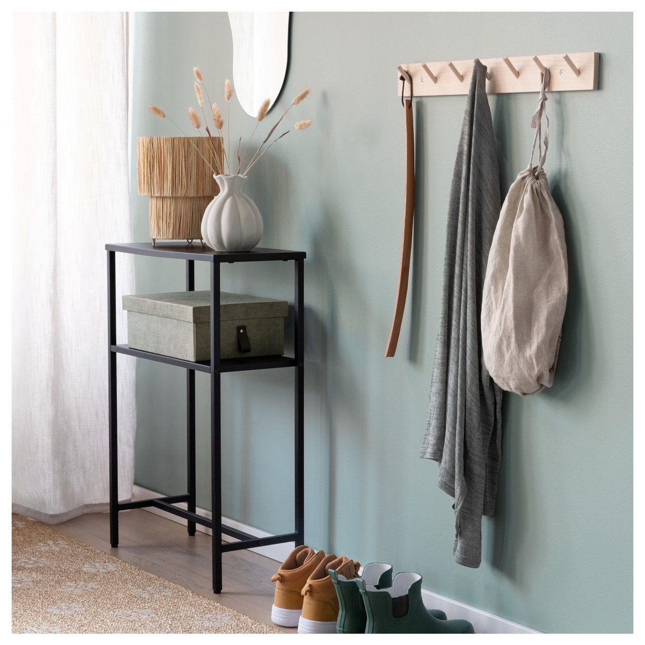 Gang med avlastningsbord, veggknagger og sko plassert ved en lys vegg med speil.