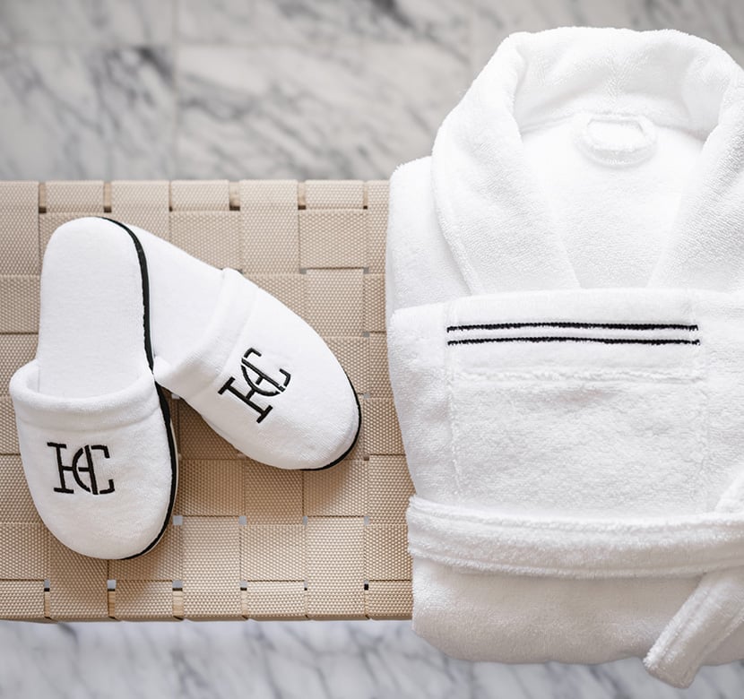 Tofflor och morgonrock från Hotel Collection på en bänk i badrumsmiljö.