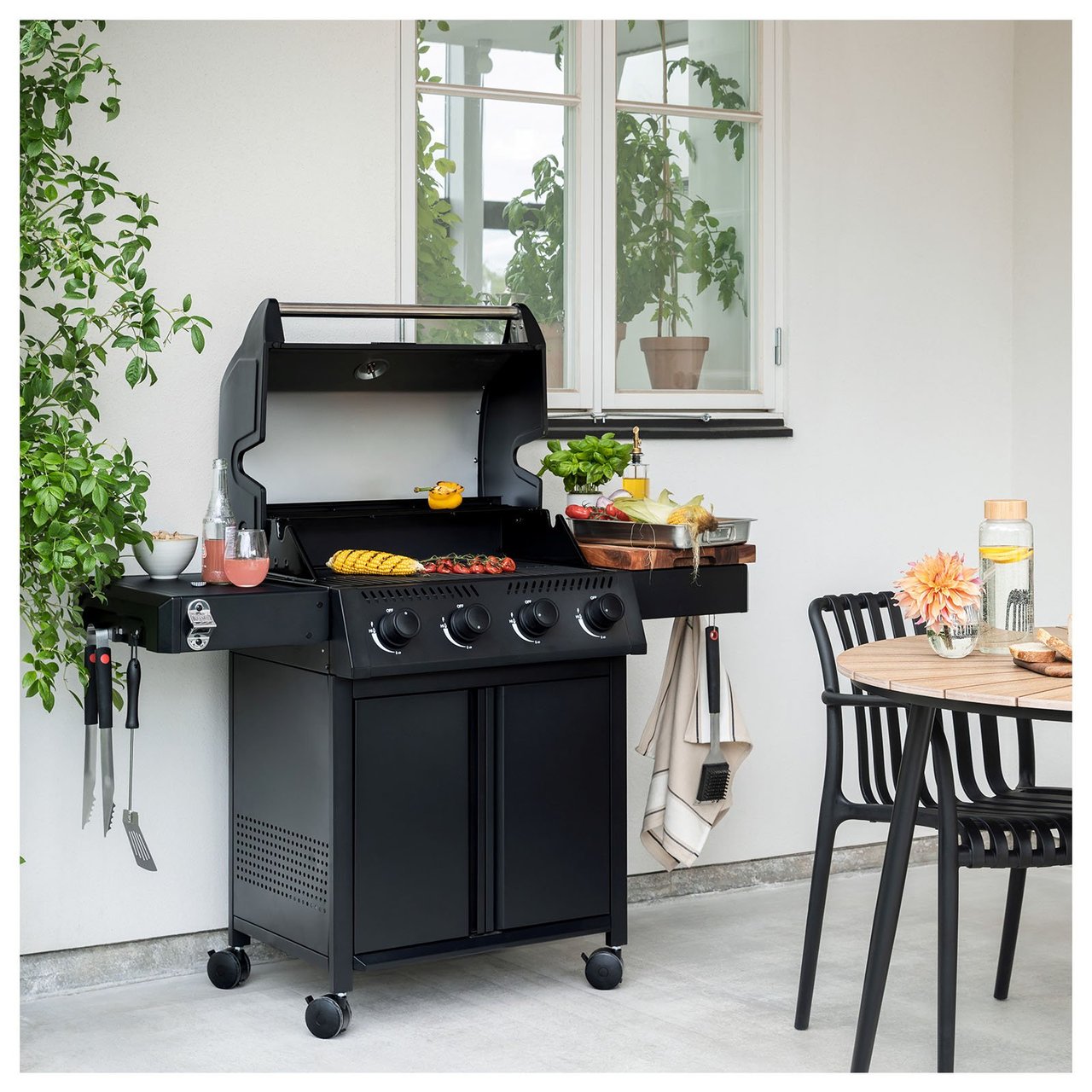 Gasgrill mit Grillgut auf dem Rost, neben einem Esstisch.