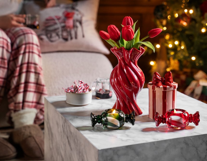 Rote Vase mit roten Tulpen, dekorative Bonbons aus Glas und Weihnachtsdeko in Form eines Geschenks auf einem Couchtisch.