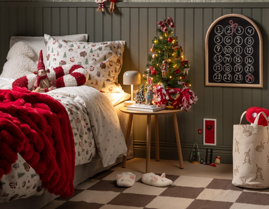 Weihnachtliches Schlafzimmer mit Weihnachtsbettwäsche, roter Decke, kleinem Weihnachtsbaum und Adventskalender.