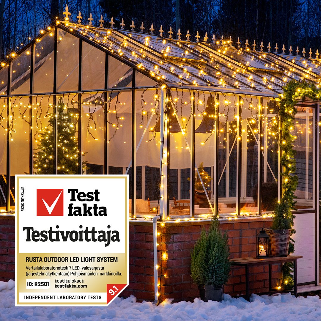 Kasvihuone ulkovalaistuksella talvisessa puutarhaympäristössä ilta-aikaan, mukana Testfakta-logo.