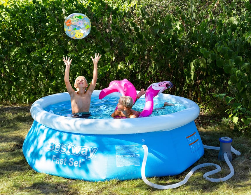 Barn leker i uppblåsbar pool i trädgård med badboll och rosa flamingoflotte en solig sommardag.