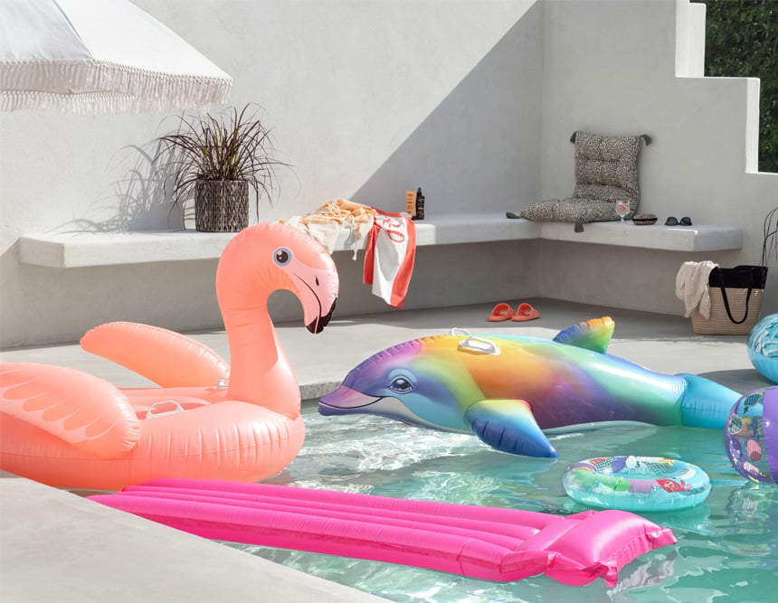 Somrig poolmiljö med uppblåsbar flamingo, färgglad delfin och badmadrass i soligt poolområde.