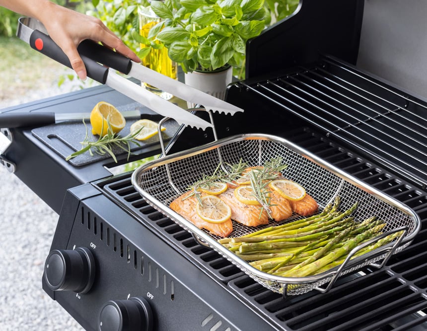 Laxfiléer och sparris grillas i grillkorg på gasolgrill, med citron och färska örter bredvid.