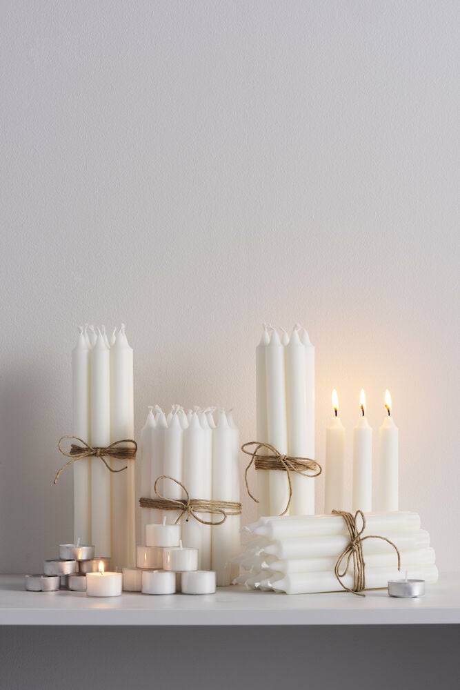 Flera vita värmeljus och stearinljus på hylla.