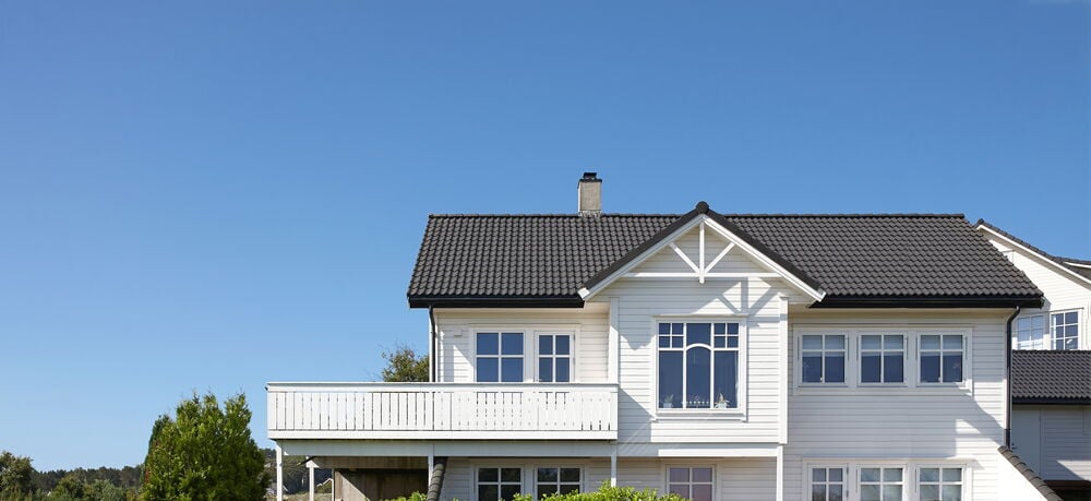 Valkoinen kaksikerroksinen talo mustalla katolla ja suurella verannalla.