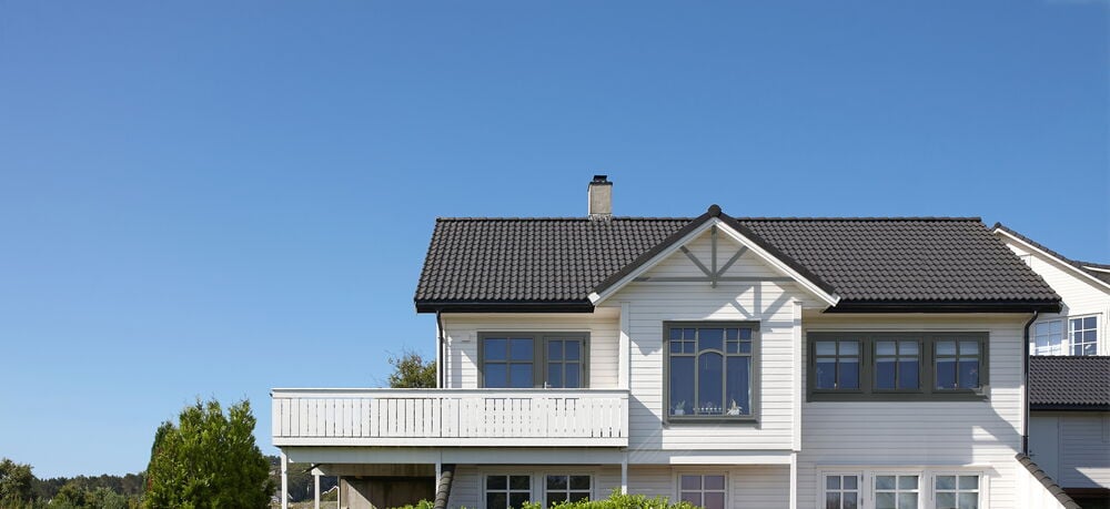 Valkoinen talo, harmaat ikkunat sinistä taivasta vasten.