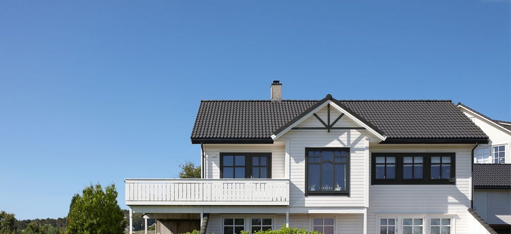 Valkoinen puutalo, jossa on tummanharmaat ikkunat ja sininen taivas.