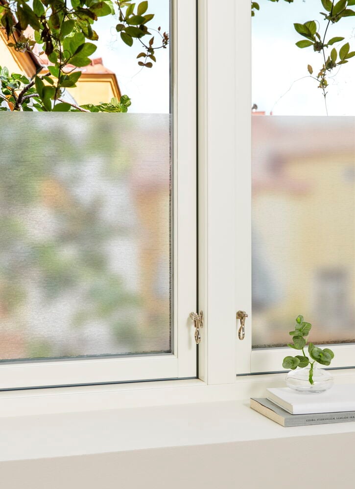 Ikkuna puoliksi läpinäkyvällä näkösuojalla ja valkoisella ikkunakehyksellä.