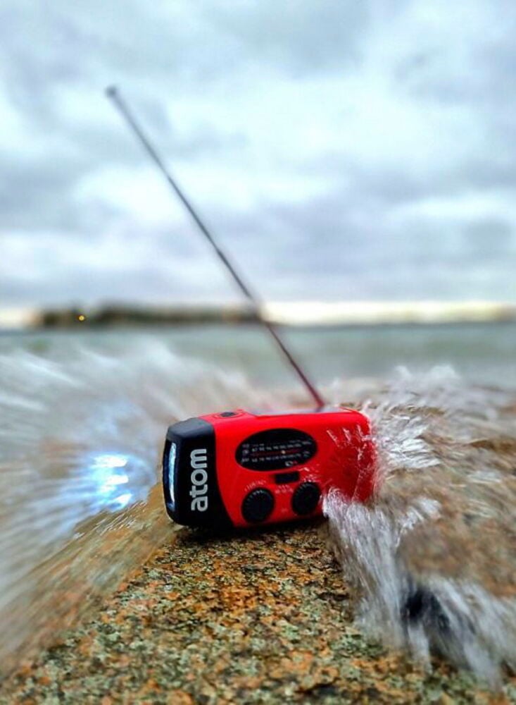 Punainen hätäradio, jossa on antenni kiven päällä veden äärellä.