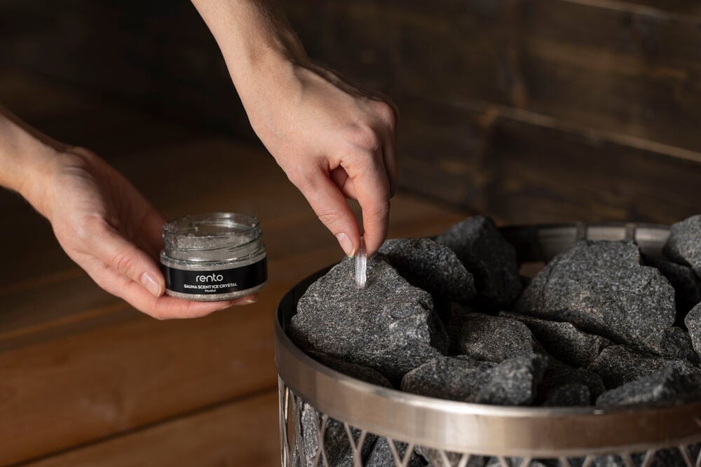 Käsi asettaa mentolikristallin lasipurkista saunan kiville.