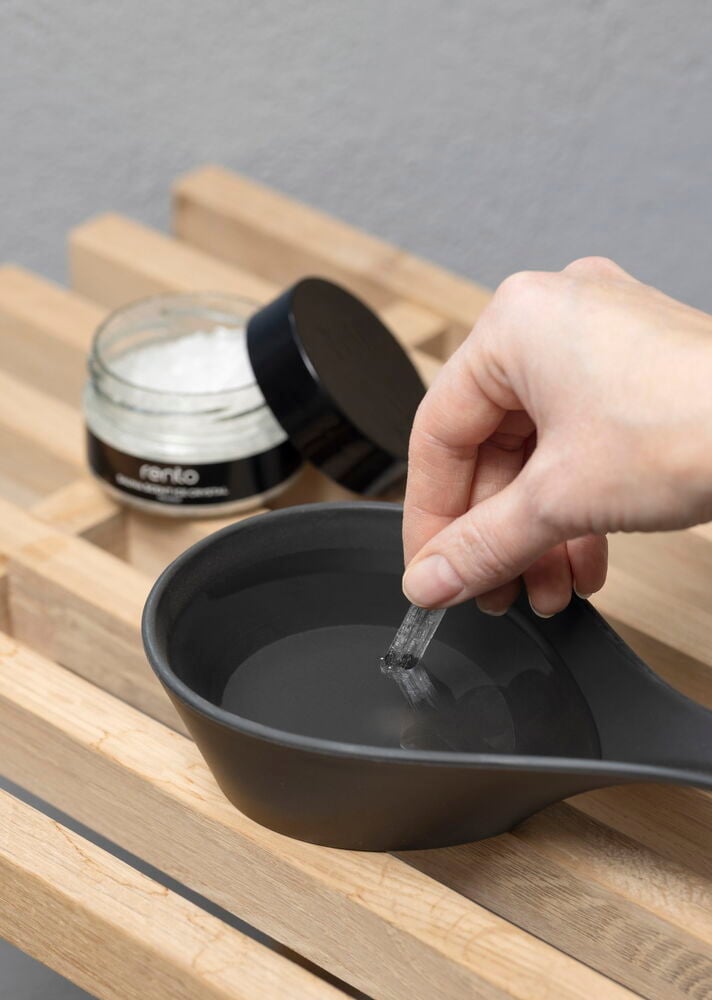 Käsi pitää mentolikristallia mustan vesikulhon yläpuolella.