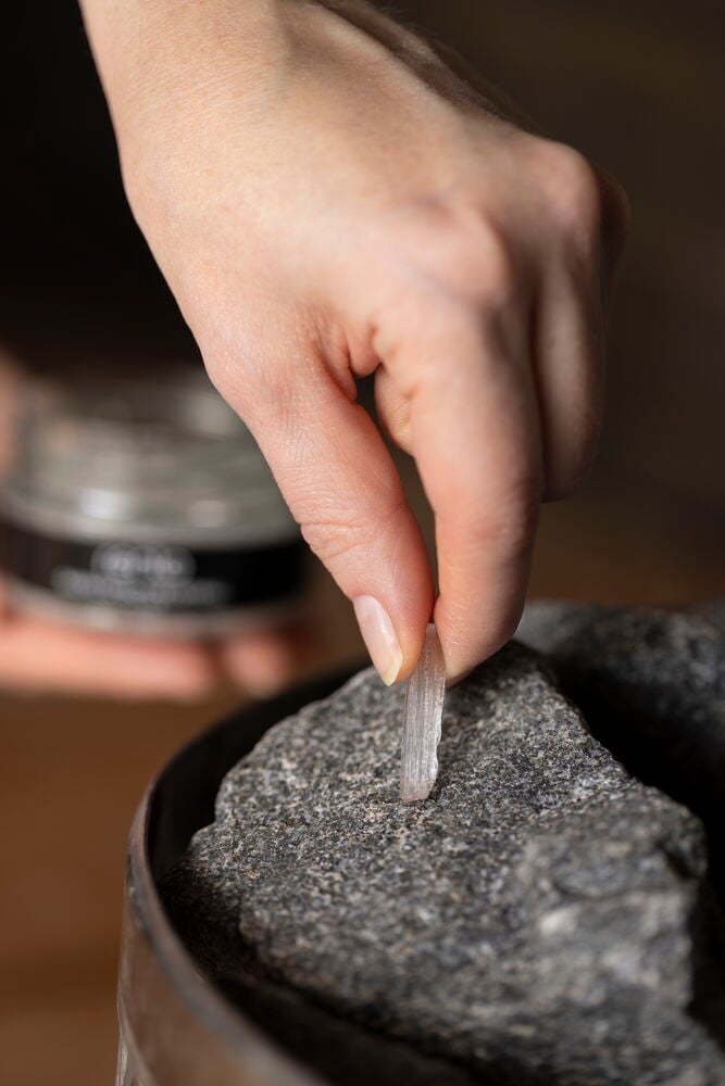 Käsi asettaa mentolikiteen kiuas kivelle.