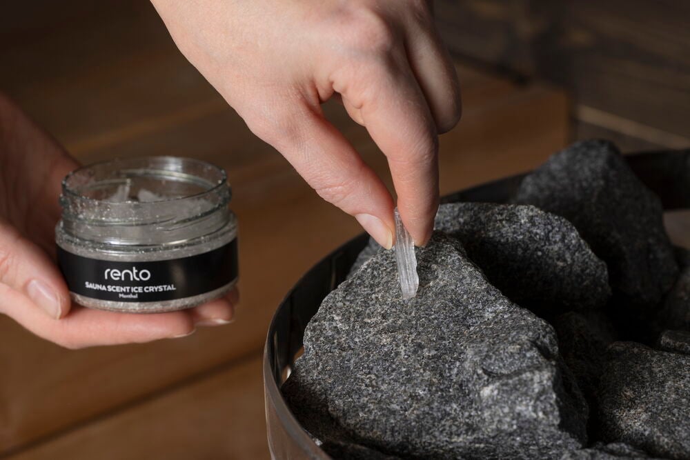 Käsi asettaa mentolikristallin purkista saunankivelle.