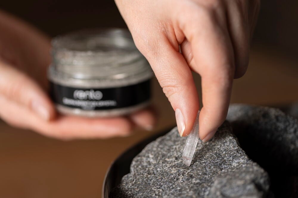 Käsi asettaa mentolikiteen sauna-kiven päälle purkista.