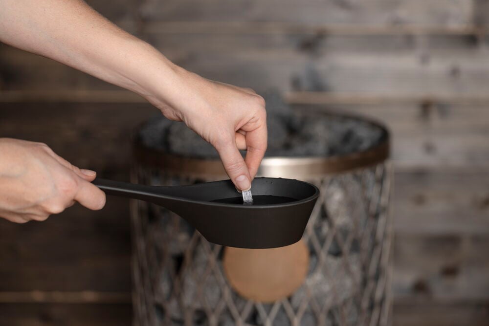 Käsi asettaa mentolikiteen kauhaan saunan kiukaan eteen.