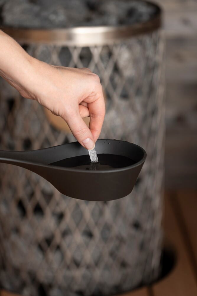 Käsi asettaa mentolikristallin saunan kauhaan vedellä.