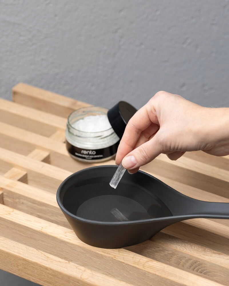 Käsi sijoittaa mentolikiteen mustaan saunakauhaan, jossa on vettä.