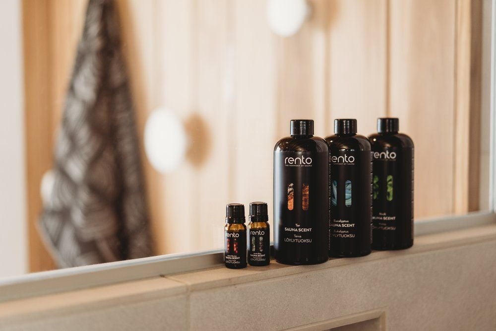 Neljä mustaa saunatuoksupulloa seisoo kaakeloidulla hyllyllä.