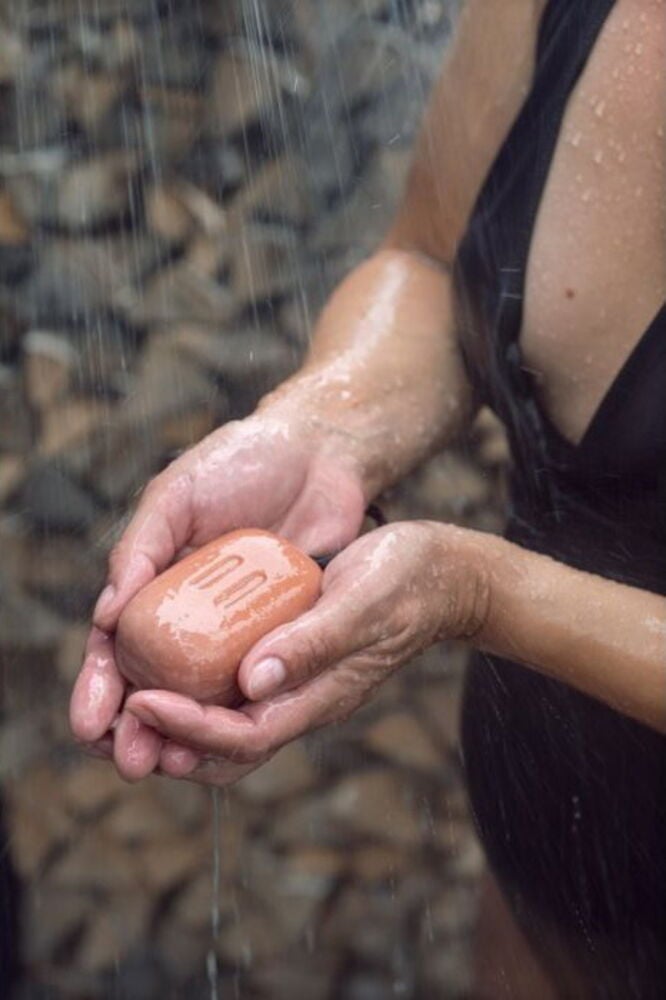 Henkilö pitää saippuaa juoksevan veden alla ulkona.