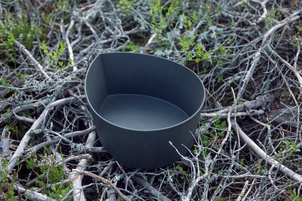 Tippamuotoinen pesuallas harmaassa värissä maassa olevilla oksilla.