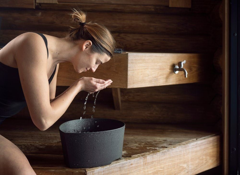 Nainen pesee kasvonsa mustan pesualtaan yllä.
