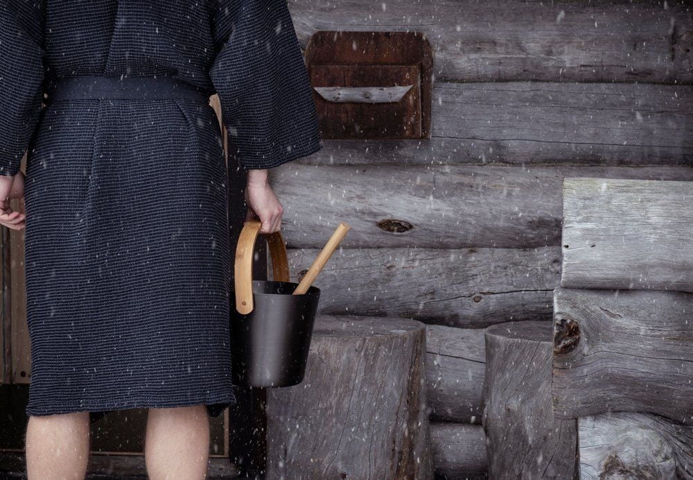 Henkilö kylpytakissa pitää saaviämpäriä ja kauhaa.