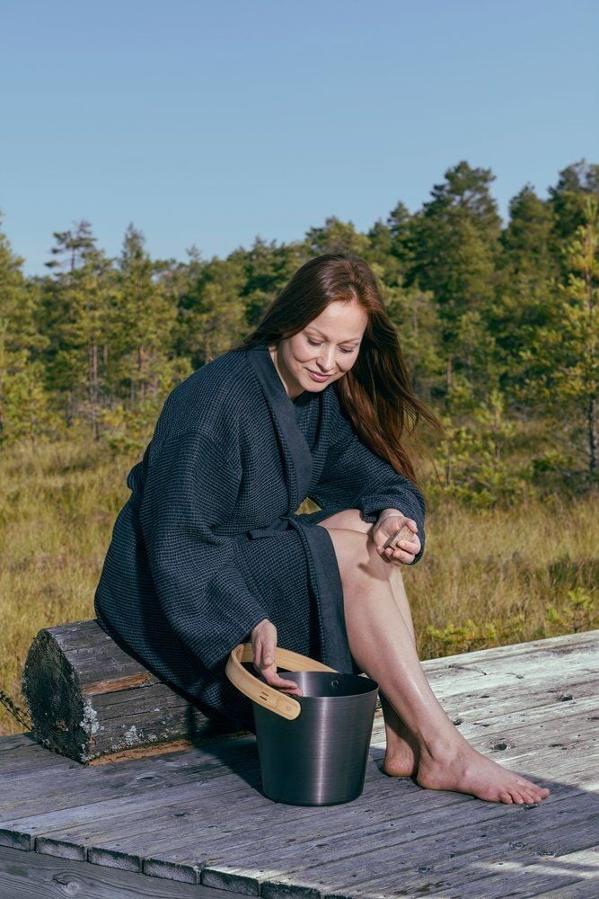 Nainen kylpytakissa ja saavi ulkona.