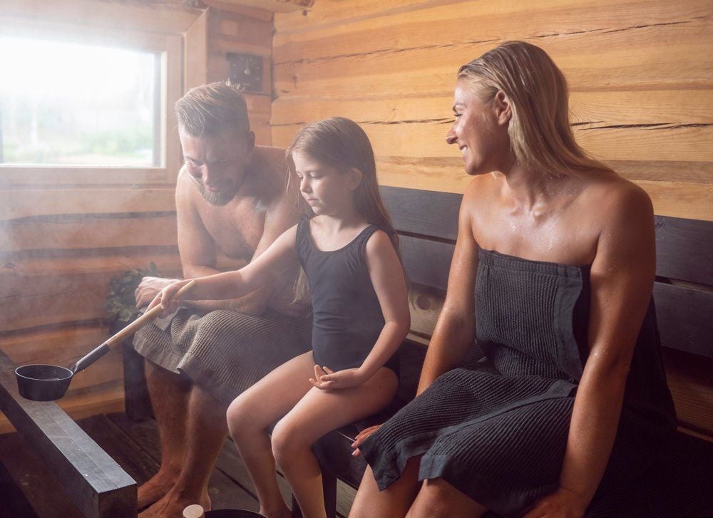 Perhe käyttää saunakiulua puusisustetussa saunassa.