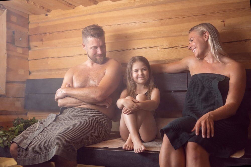 Perhe istuu yhdessä saunassa puisella istuimella.