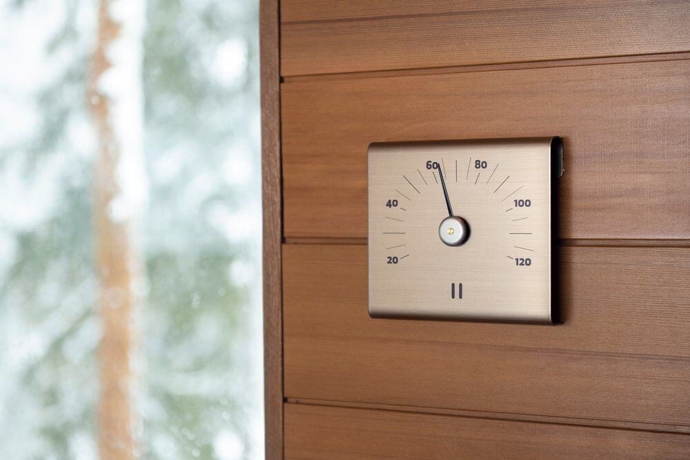 Shampanjanvärinen saunatermometri alumiinista puuseinällä.