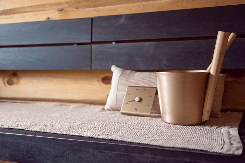 Samppanjanvärinen saunamittari ja ämpäri saunapenkillä.