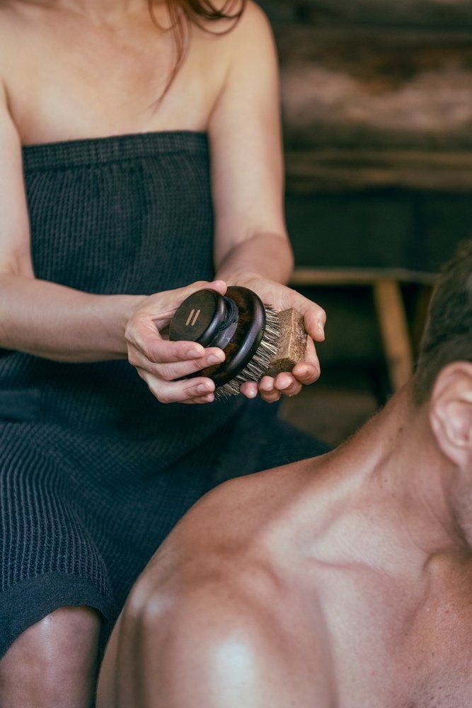 Nainen pitää soikeaa vartaloharjaa miehen selkää vasten.