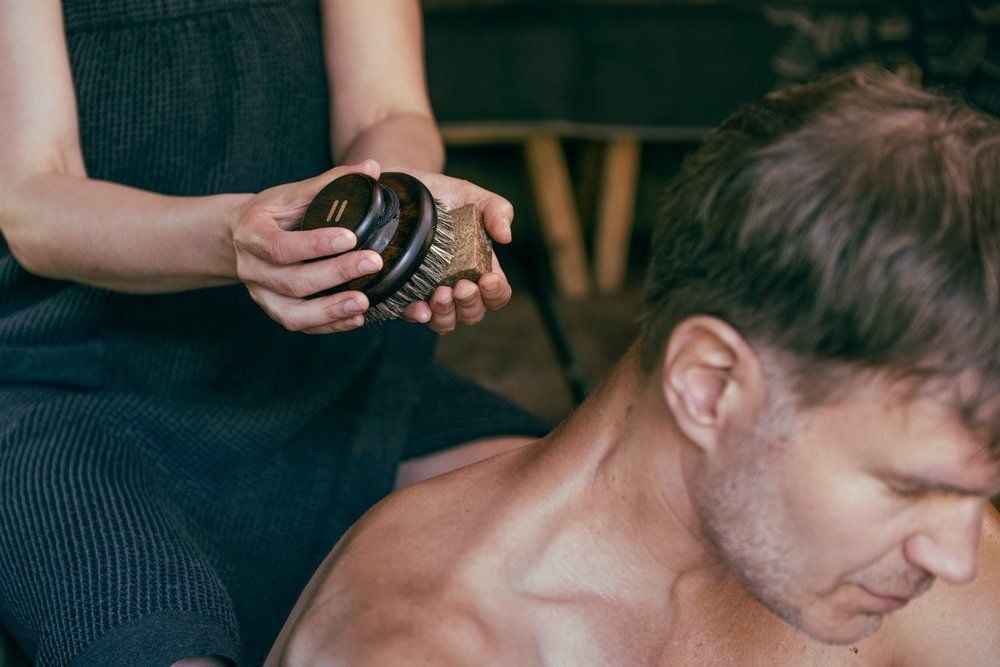 Henkilö käyttää ovaalia vartaloharjaa paljaalla selällä.