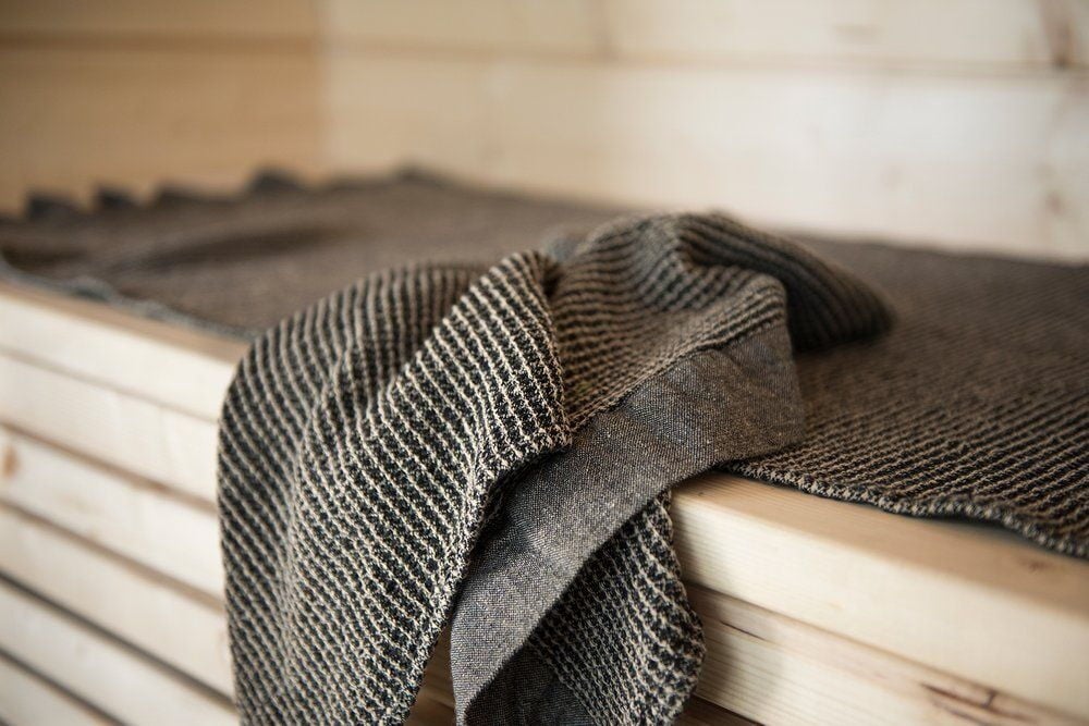 Mustavalkoinen ja beige saunapeitto vaalealla puupenkillä.