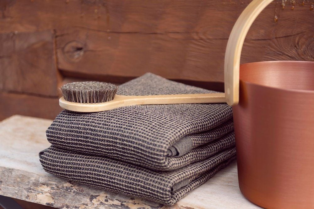 Kaksi taiteltua mustaa saunanlaudeliinaa, harja ja ämpäri.