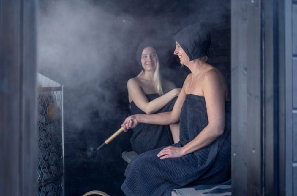 Kaksi naista saunassa tummissa saunahatuissa.