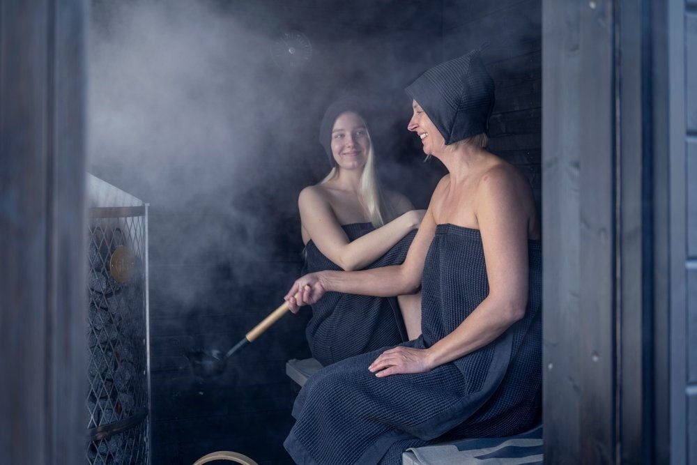 Kaksi naista saunassa, yhdellä musta saunahattu.
