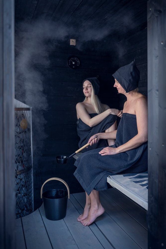 Kaksi henkilöä saunahatuissa pimeässä saunassa.